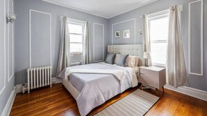 Un dormitorio con cama, mesita de noche y ventana con cortinas.