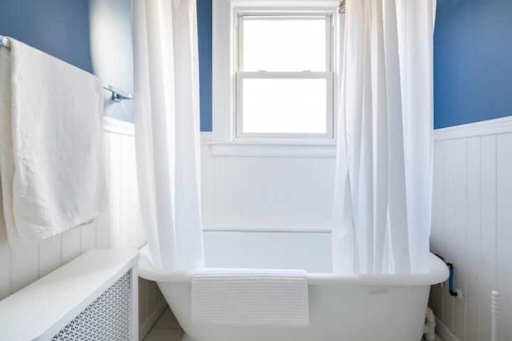 Een badkamer met een bad, een raam en een witte douchegordijn.