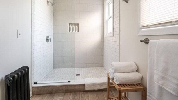 Un baño moderno con ducha envuelta en vidrio, un banco de madera y un perchero para toallas.