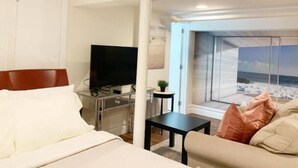 Habitación de hotel con cama, televisor, mesita, sofá y ventana con vista a la playa.