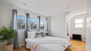 A bedroom with a bed, curtains, a radiator, and a potted plant.