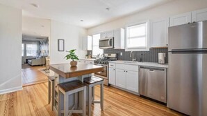 A modern kitchen with white cabinets, stainless steel appliances, and a wooden dining table.