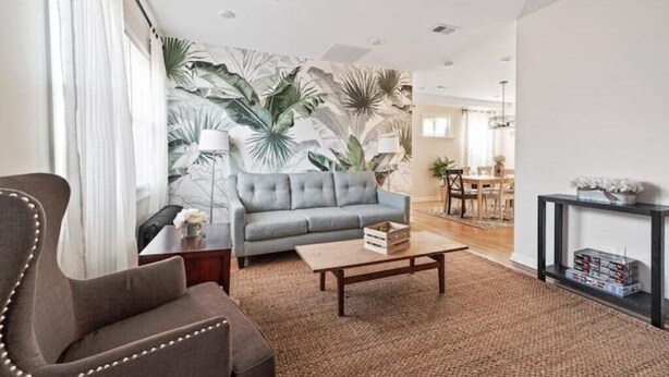 A living room with a grey sofa, a brown armchair, a wooden coffee table, and a patterned wall.