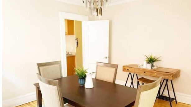 A dining room with a dark wooden table, white chairs, and a small wooden side table with plants. - 2-BDR Oasis Near Beth Isreal Hosp 10 mins to EWR (Newark)