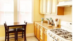 A kitchen with wooden cabinets, a stove, and a dining table with chairs. - 2-BDR Oasis Near Beth Isreal Hosp 10 mins to EWR (Newark)