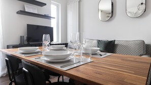 A dining table set with white plates, glasses, and cutlery, a black chair, a sofa with patterned cushions, a television, and a mirror on the wall. - Italianway Comfort - Buenos Aires 65 E (Milan)