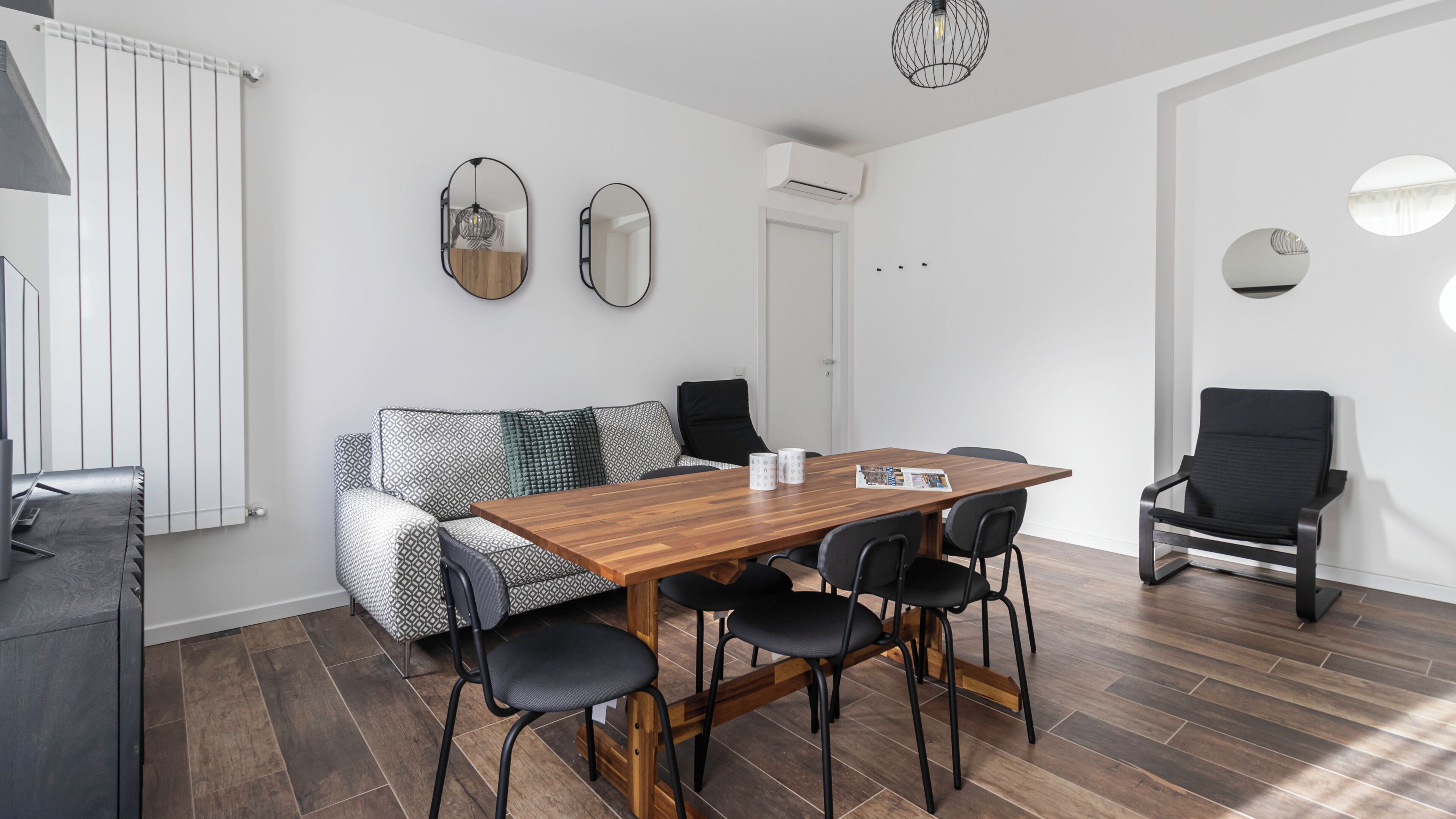 A modern room with a wooden dining table, black chairs, a patterned sofa, and a black armchair.