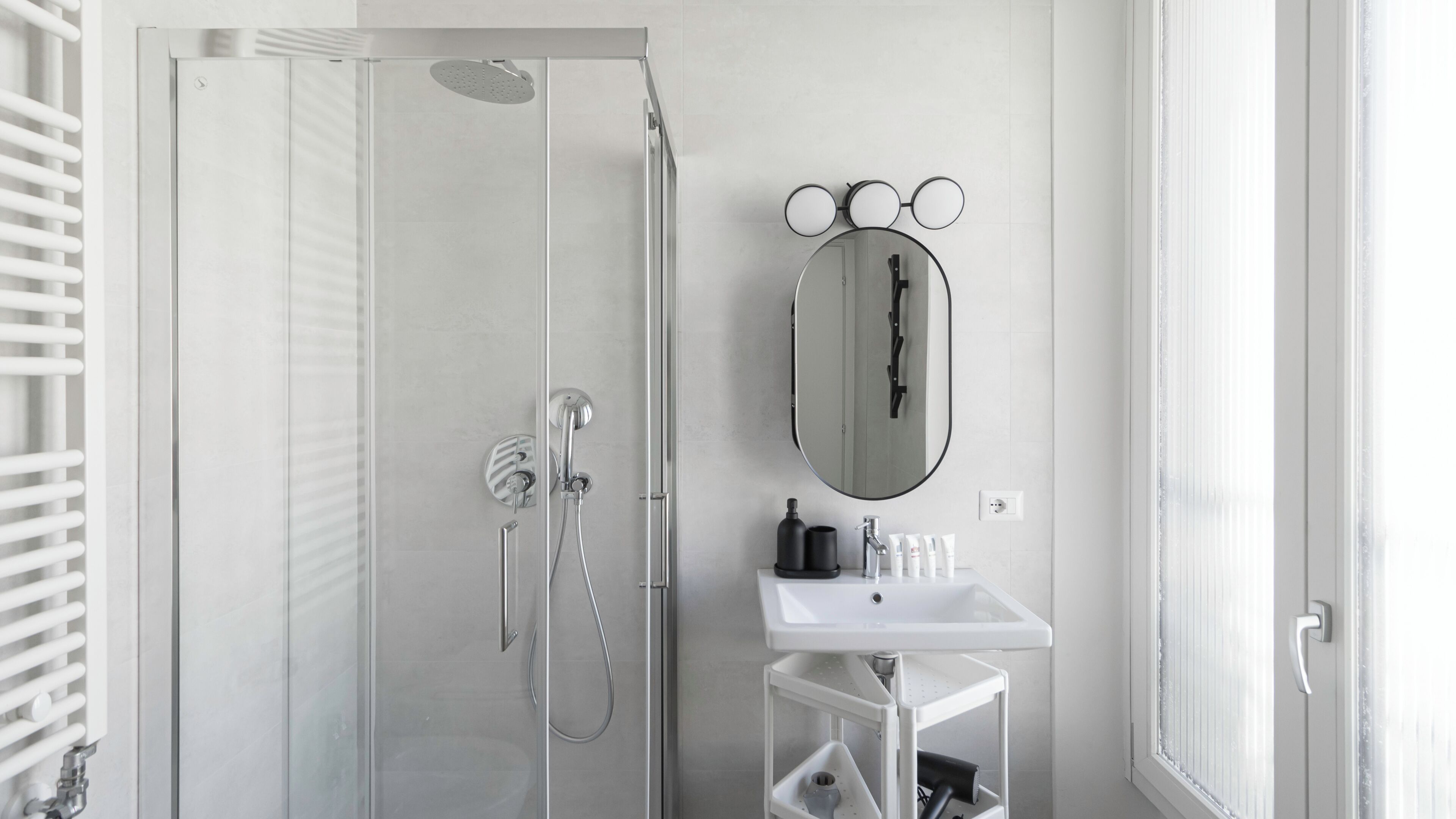 A modern bathroom with a glass-enclosed shower, a white sink, and a mirror with a round frame.