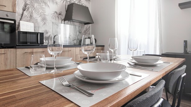 A modern dining area with a wooden table set for a meal, including bowls, wine glasses, and cutlery. - Italianway Comfort - Buenos Aires 65 E (Milan)