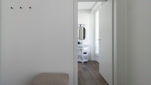A hallway leading to a bathroom with a vanity, mirror, and a bench. - Italianway Comfort - Buenos Aires 65 E (Milan)