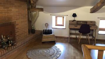 Une pièce chaleureuse avec des poutres apparentes, une cheminée en briques, un bureau avec une chaise et une grande fenêtre.