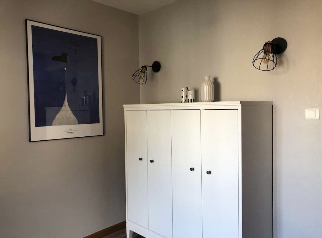 Une pièce avec une armoire blanche, un tableau encadré accroché au mur et deux appliques murales.