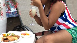 Una persona sentada en una mesa al aire libre, con un plato de comida y una bebida.