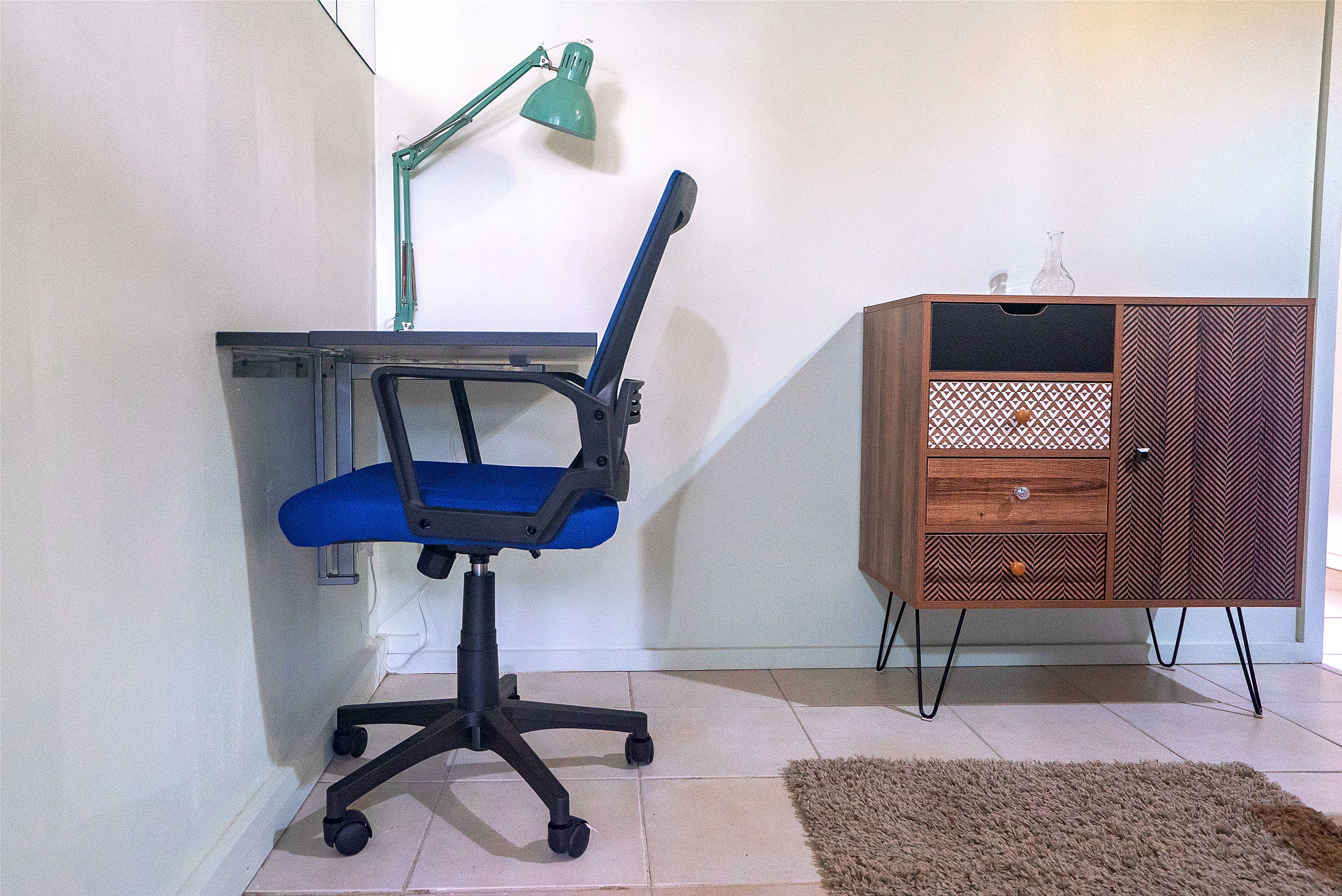 A workspace with a blue office chair, a desk, a green desk lamp, and a wooden cabinet with drawers.