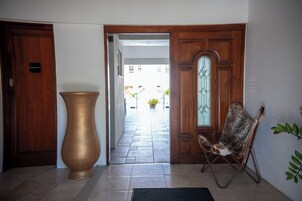Un pasillo con un gran jarrón de bronce, una puerta de madera que dice “PRIVATE” y una silla con tela estampada.