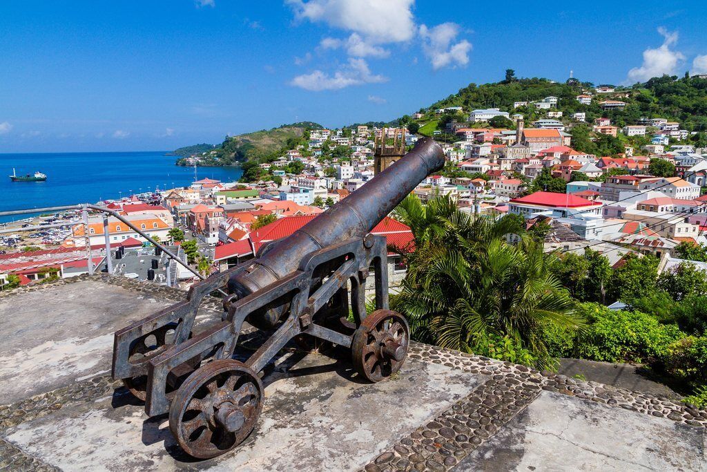 A cannon on a stone platform overlooking a coastal town with buildings and a clear blue sky.