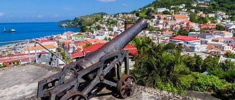 A cannon on a stone platform overlooking a coastal town with buildings and a clear blue sky.