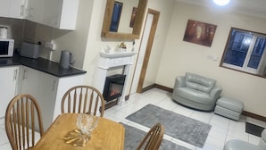 A dining area with a wooden table and chairs, a kitchen with white cabinets, a fireplace, and a grey sofa. - Beautiful 3-bed Bungalow in Bawtry Doncaster (Doncaster)
