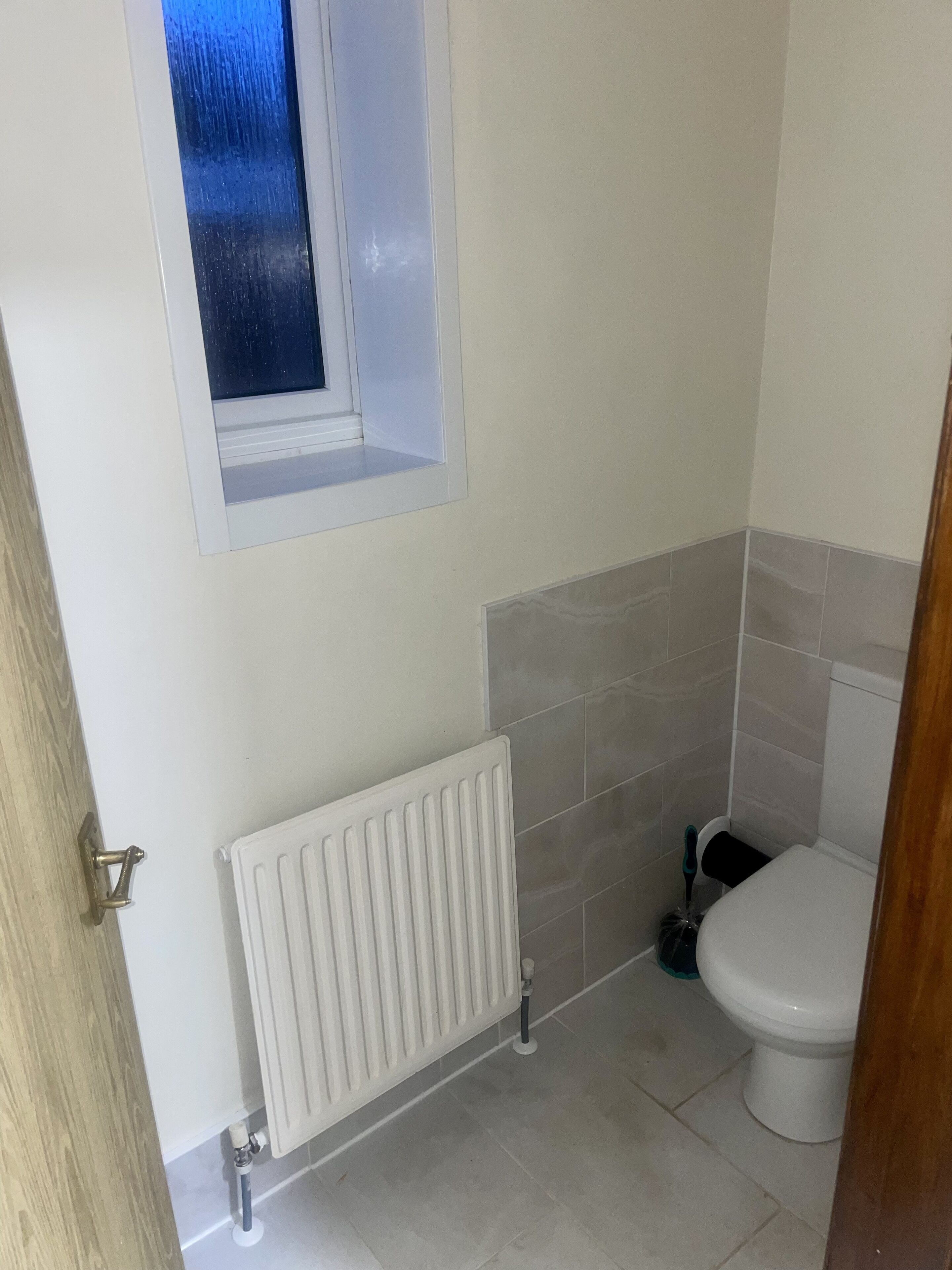 A small bathroom with a toilet, a radiator, and a window.