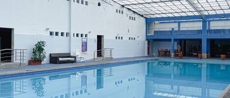 An indoor swimming pool with a glass ceiling, a bench, and a chair near the poolside.
