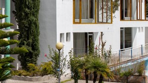 Un bâtiment moderne à l’extérieur blanc, doté de cadres de fenêtres en bois, entouré de verdure et avec une chaîne de montagnes en arrière-plan.