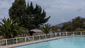 Une piscine dotée d’une terrasse carrelée, entourée d’arbres et d’une clôture blanche.