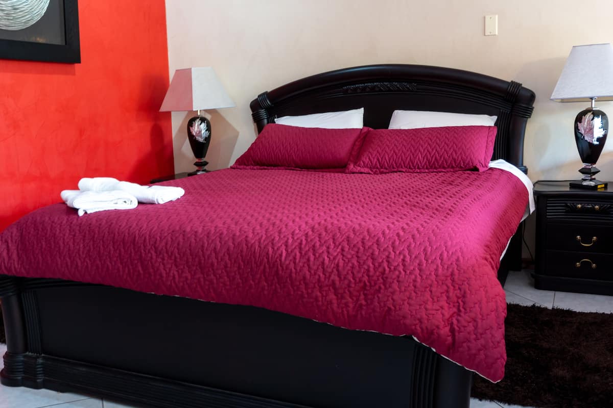 A bed with a red bedspread, two white pillows, and a white towel on the side. There are two bedside tables with lamps.