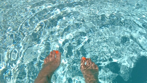 Piernas y pies de una persona en una piscina con agua cristalina.