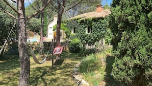 Un jardín con una hamaca, un sendero de piedra y una casa con muros cubiertos de hiedra.