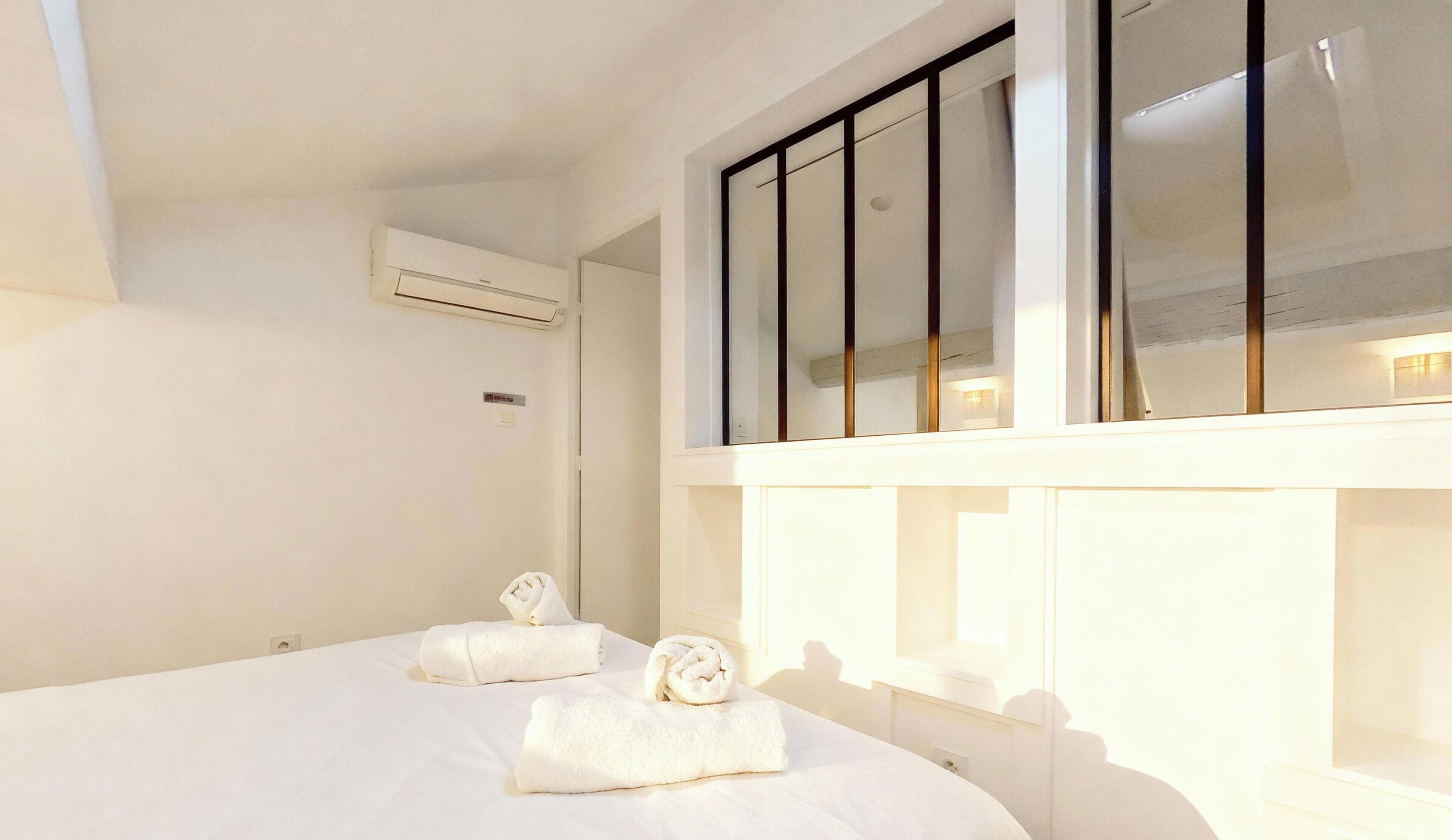 Een hotelkamer met een groot bed, twee opgerolde handdoeken, een airconditioning en een raam met jaloezieën.