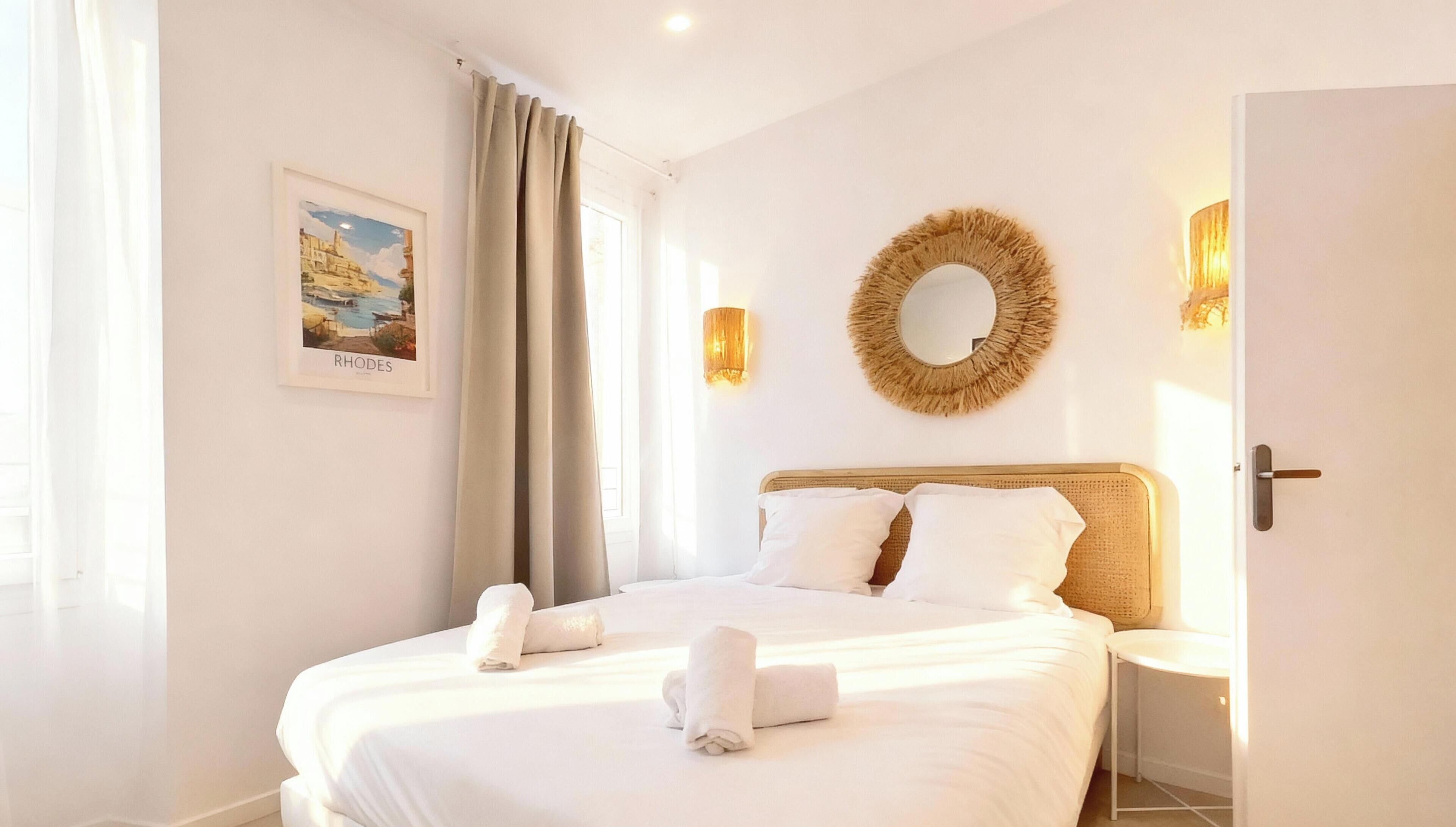 Habitació d'hotel amb un llit, una fotografia emmarcada de Rhodes, un mirall rodó i una porta.