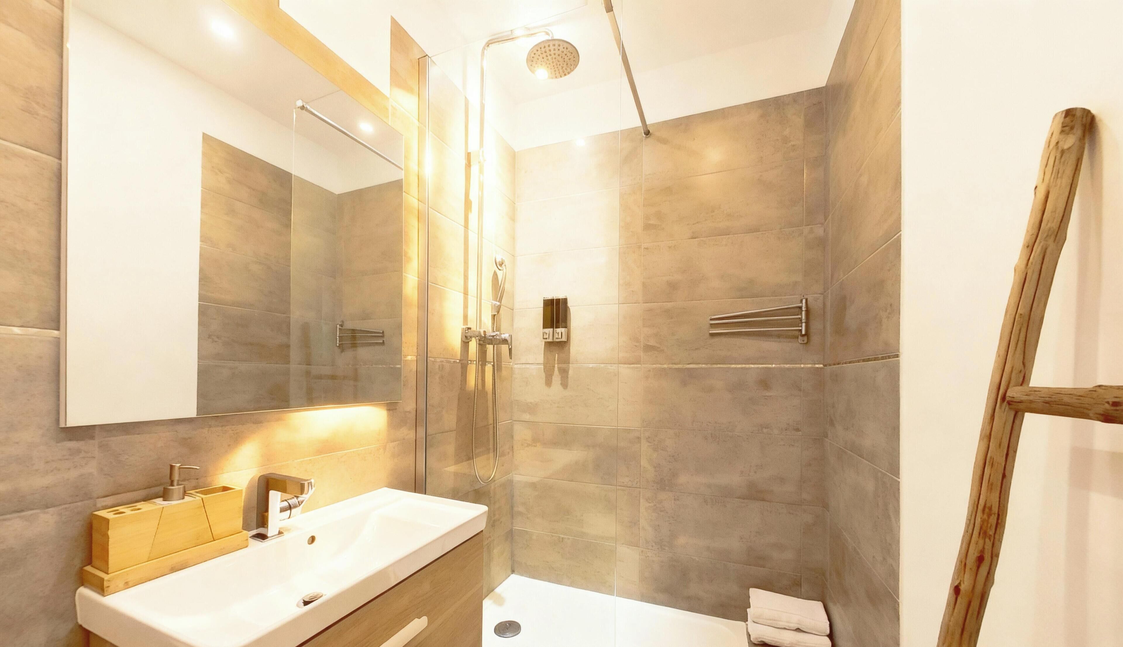 A modern bathroom with a large mirror, a shower with a handheld showerhead, and a vanity with a sink and soap dispenser.