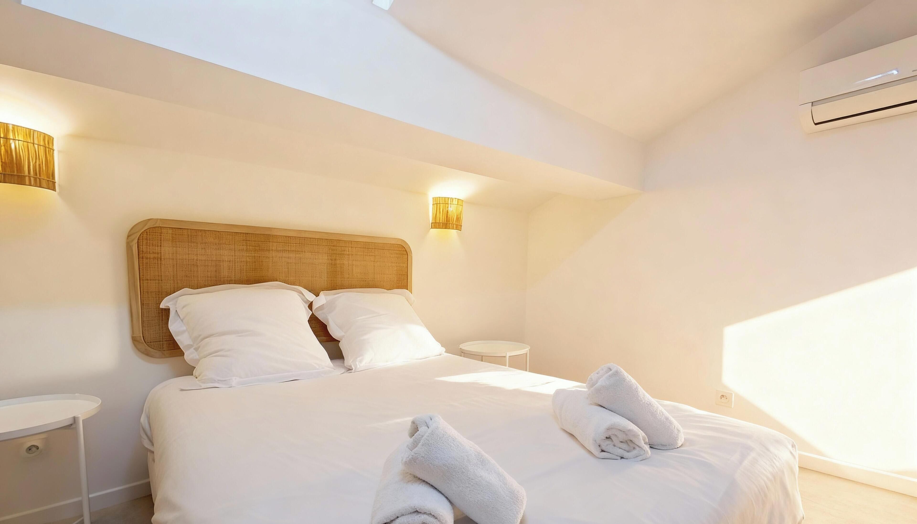 A hotel room with a large bed, two bedside tables, a wall-mounted lamp, and an air conditioning unit.