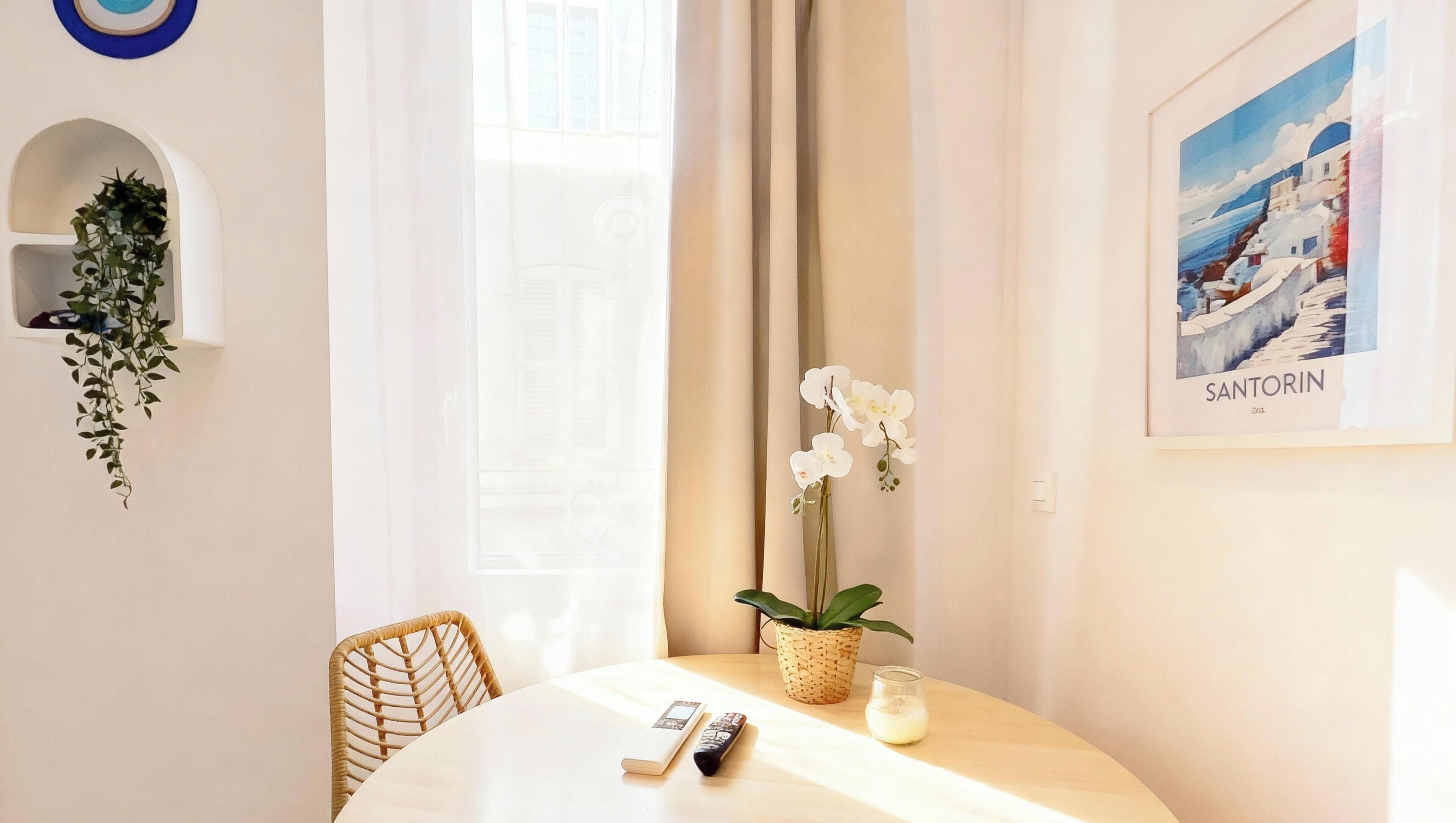 Un área de comedor con una mesa redonda, sillas, un control remoto, un libro, una vela y una planta en maceta.