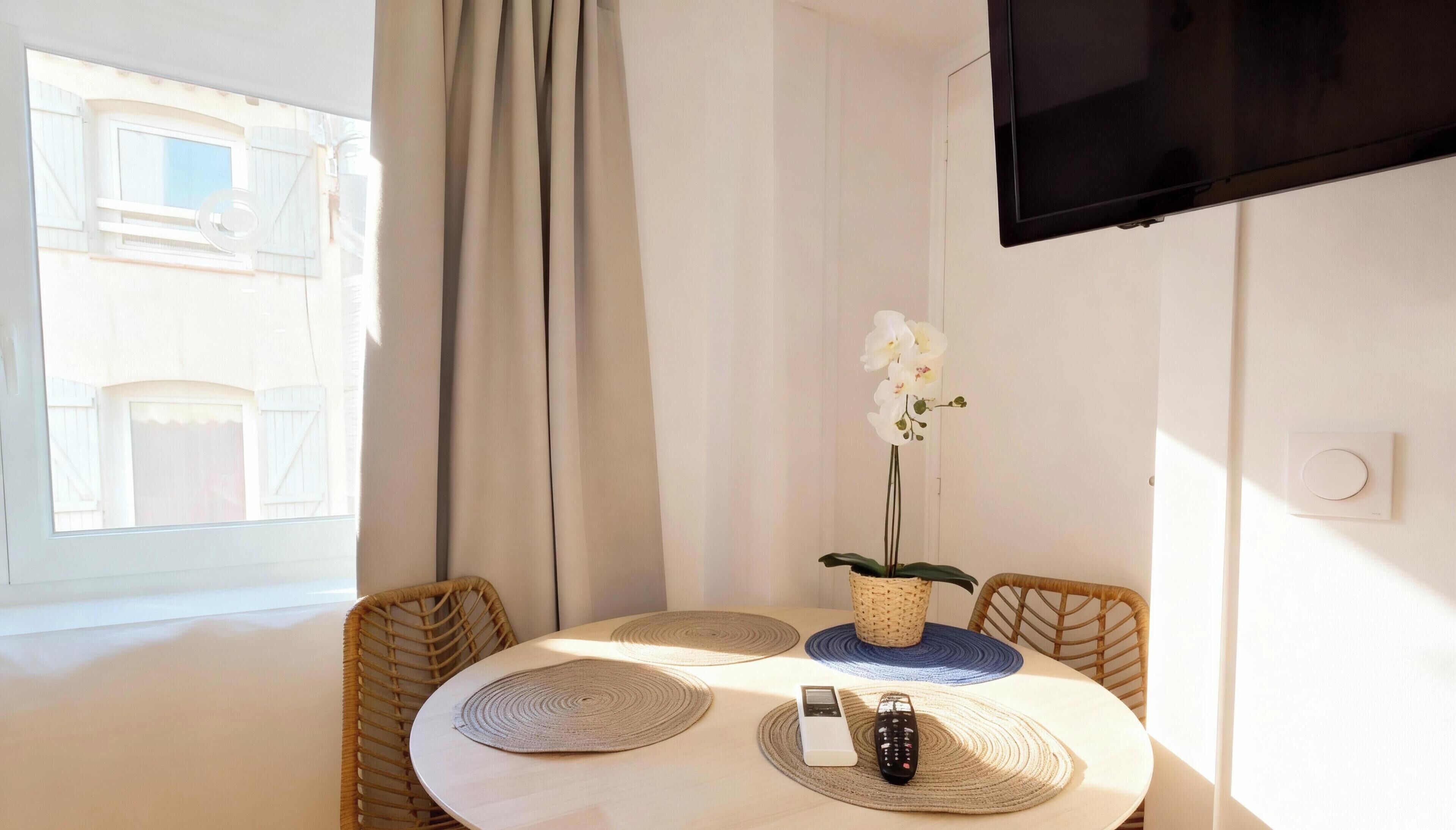 Een kamer met een eettafel, stoelen, een televisie en een raam met gordijnen.