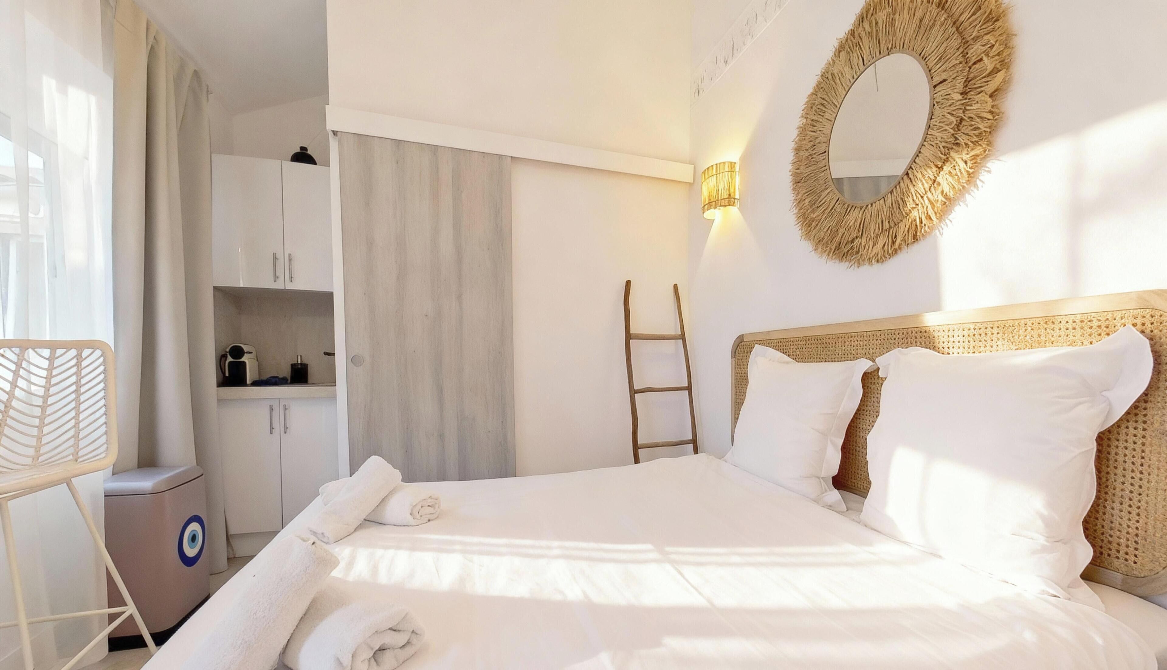 A neatly made bed with white linens, a wooden headboard, and a wall-mounted mirror.