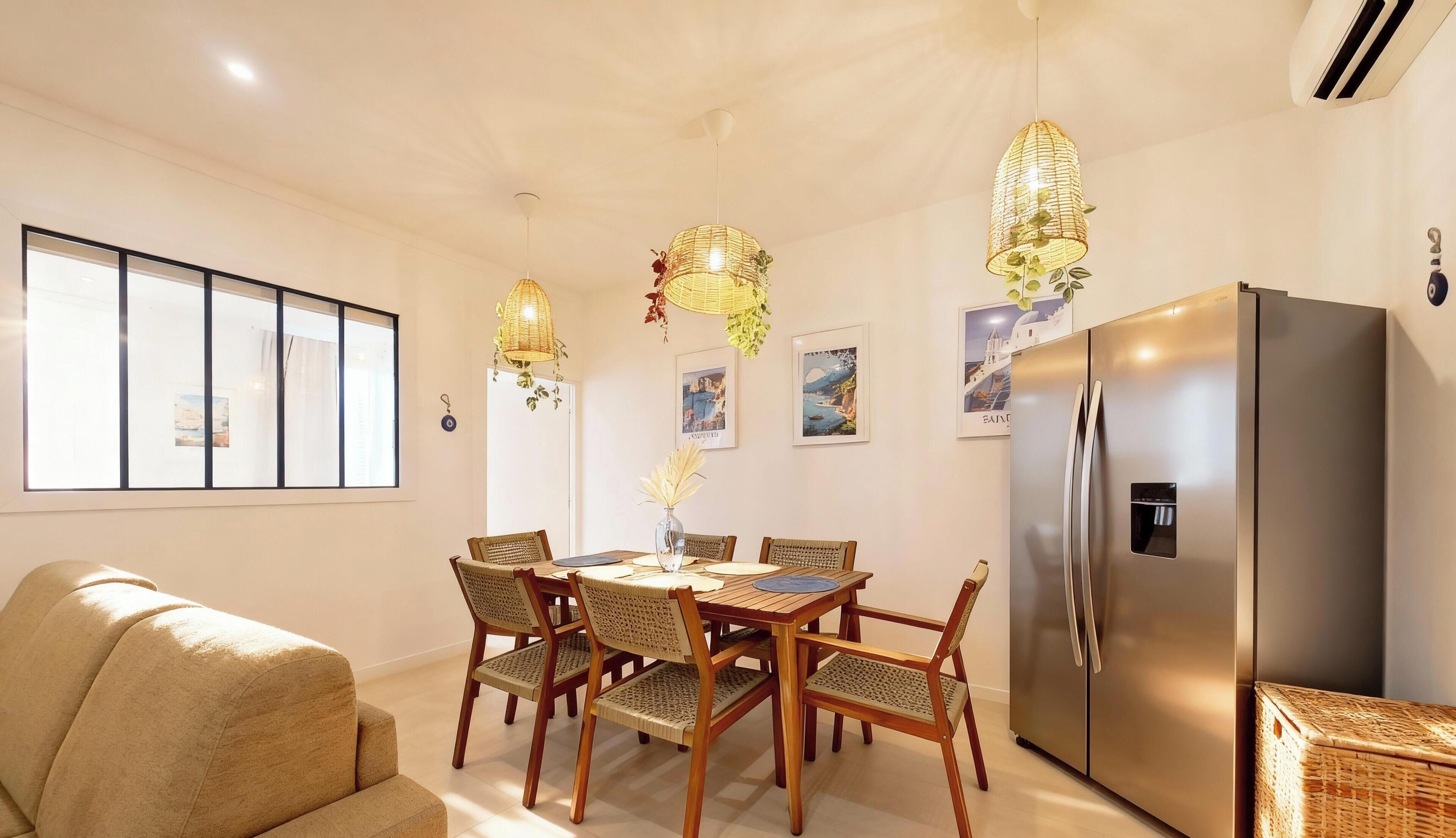 A dining area with a wooden table, four chairs, a sofa, and a stainless steel refrigerator.