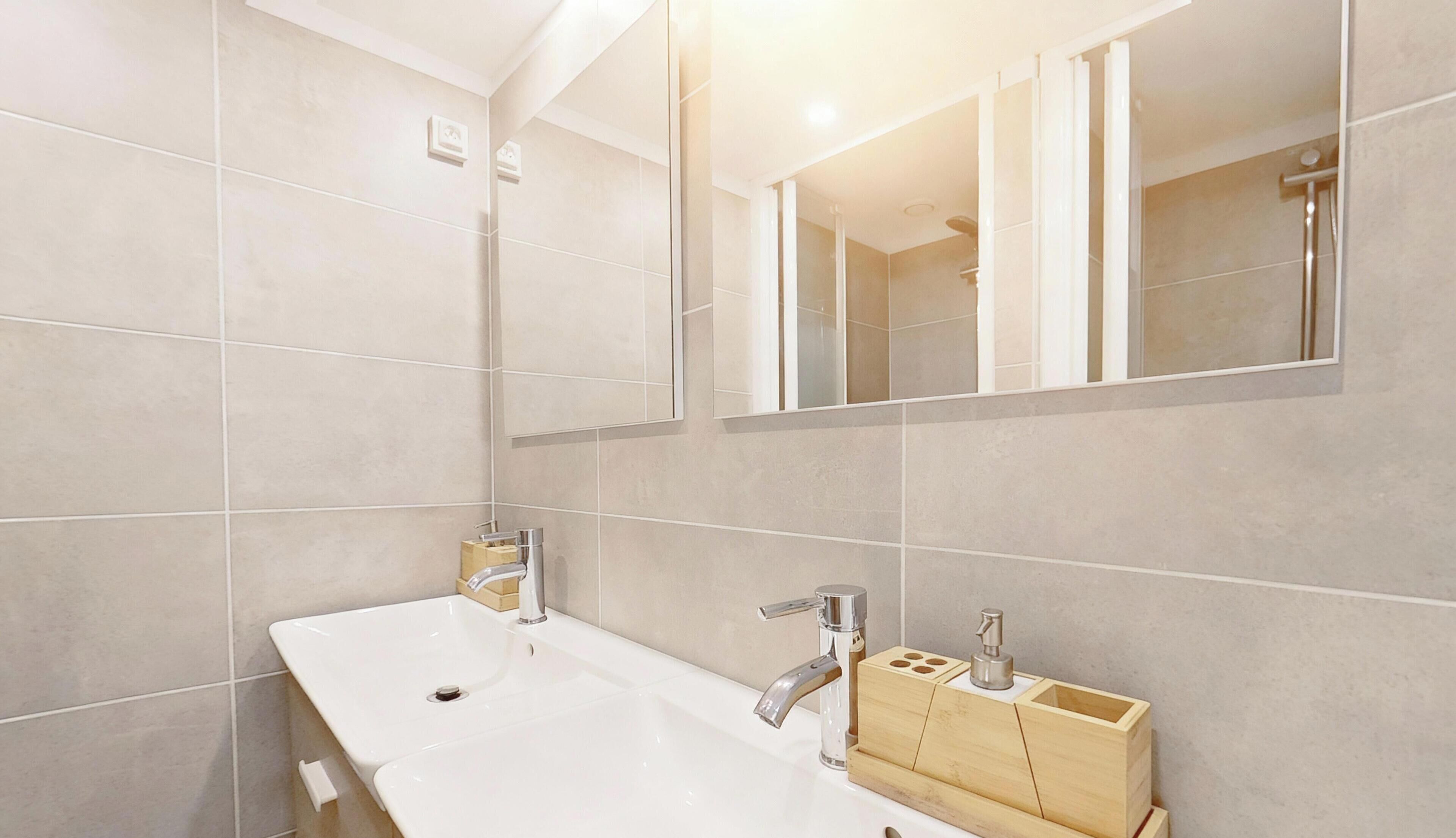 A modern bathroom with two sinks, a large mirror, and a shower area.