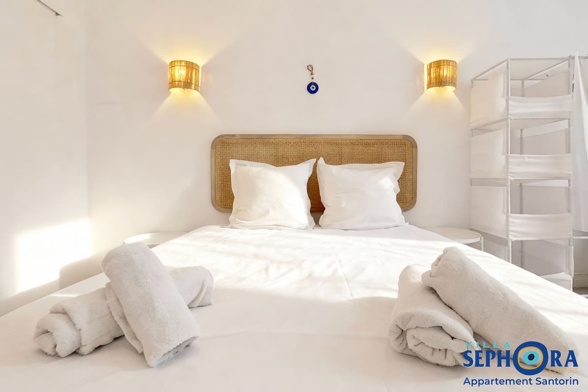 A clean, modern bedroom with a white bed, two wall-mounted lamps, and a wicker headboard.