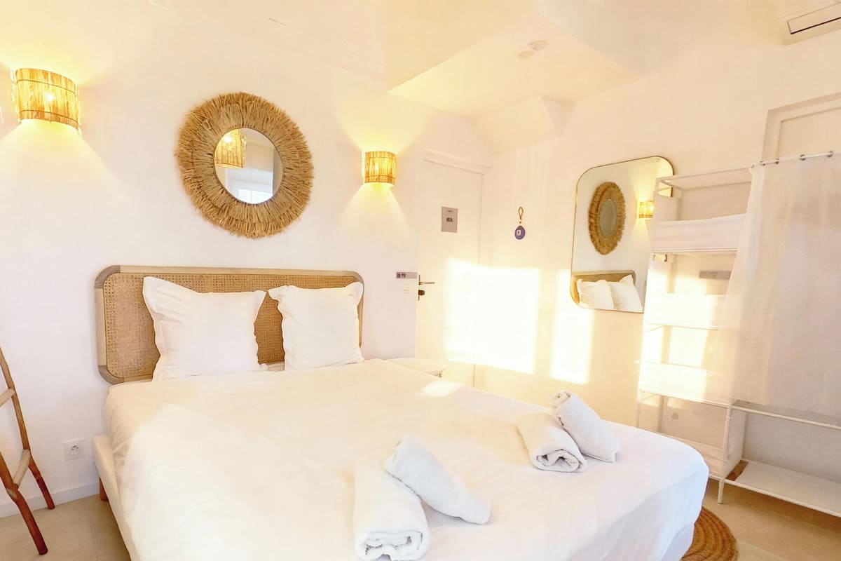 A well-lit bedroom with a large bed, two wall-mounted lamps, a mirror, and a wooden ladder.