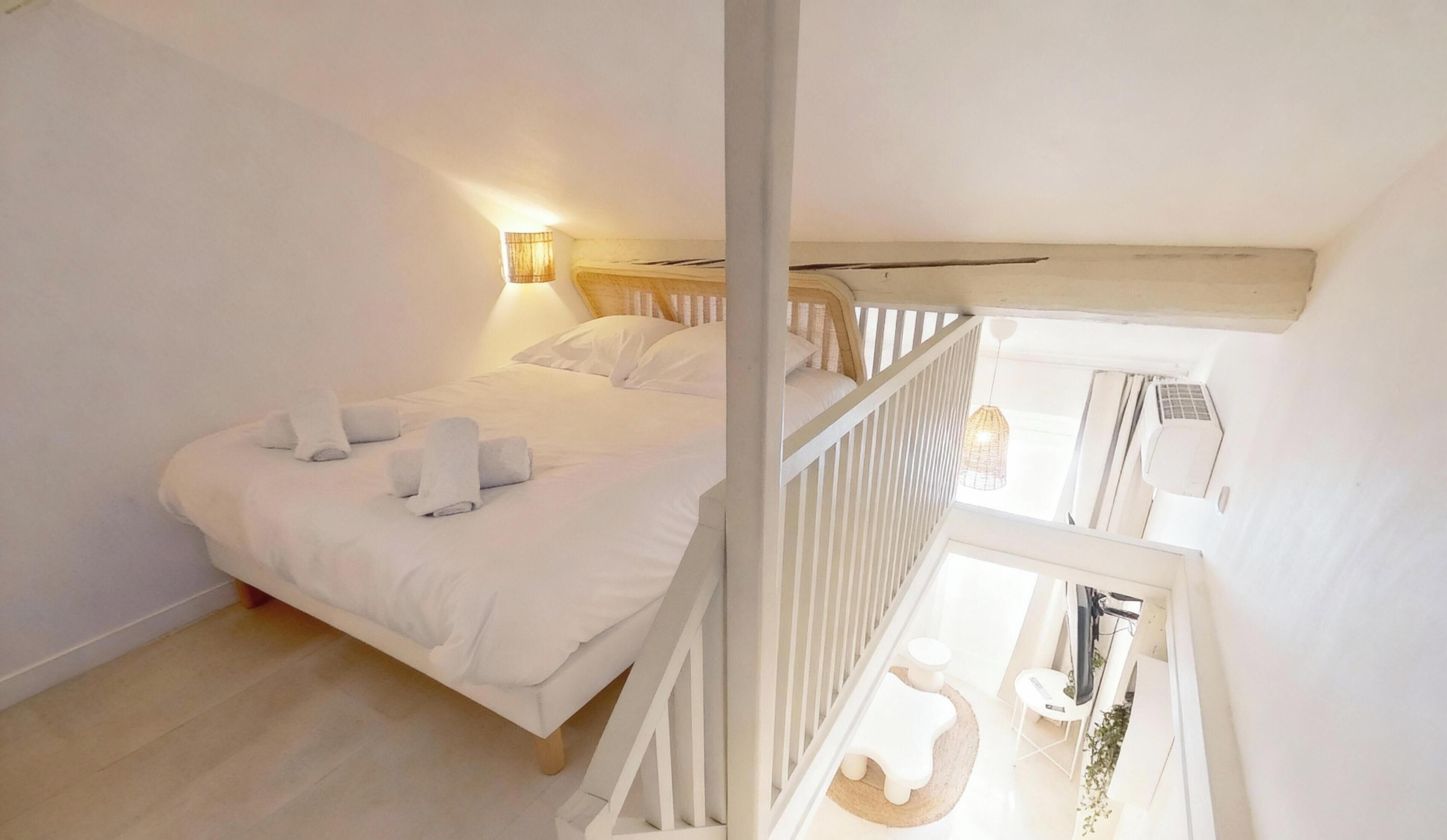 Une chambre à coucher avec un lit, des serviettes blanches, une table de chevet, une lampe et une vue sur le balcon.