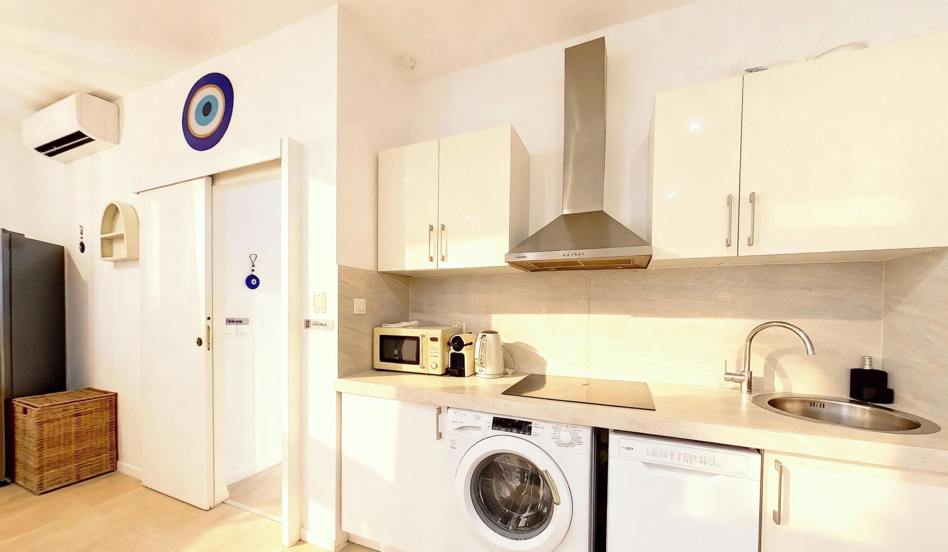 A compact kitchen with a washing machine, microwave, and a sink.