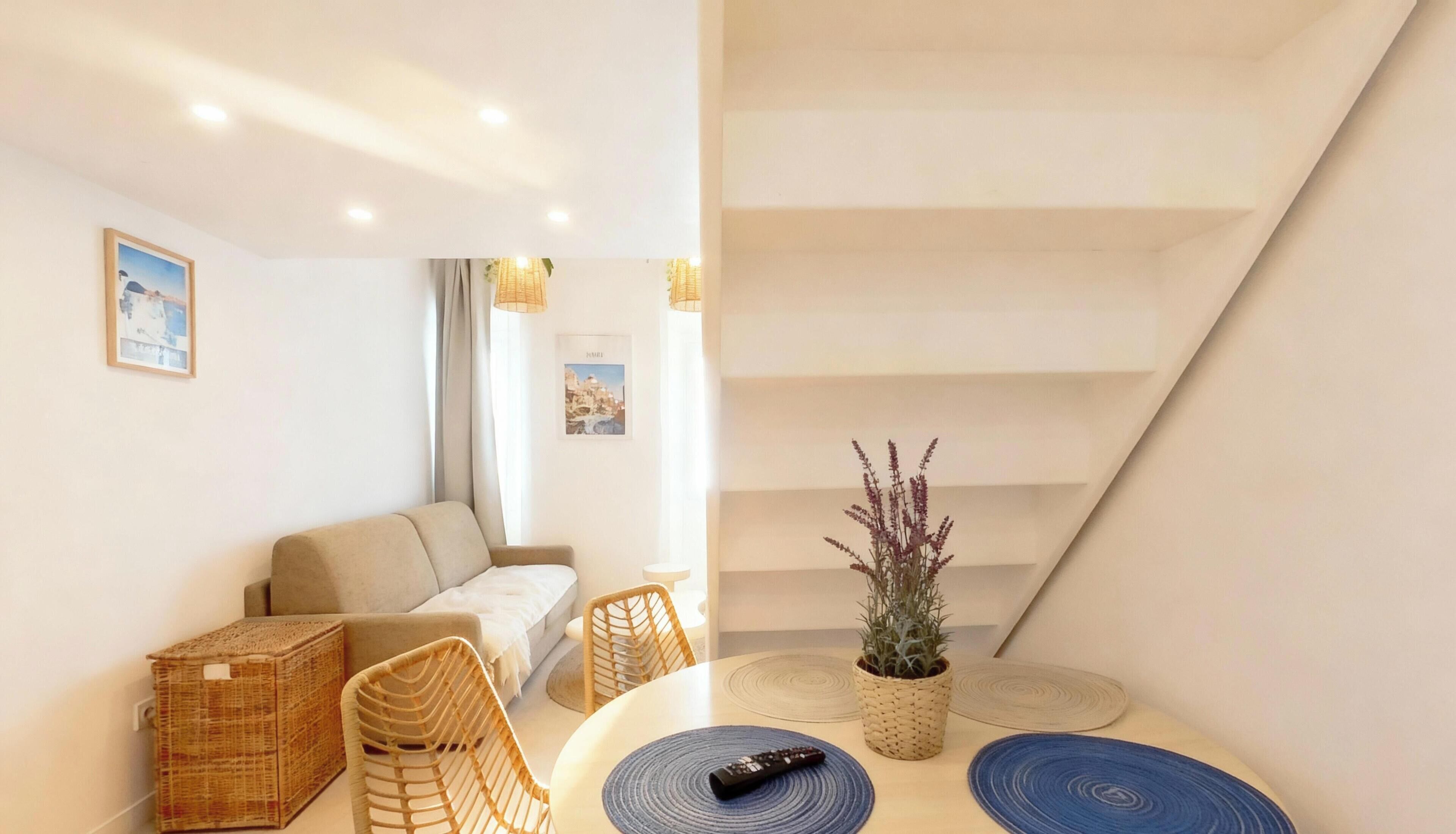 Un salon moderne avec un canapé, une table à manger et des chaises, une plante en pot et une télécommande posée sur la table.
