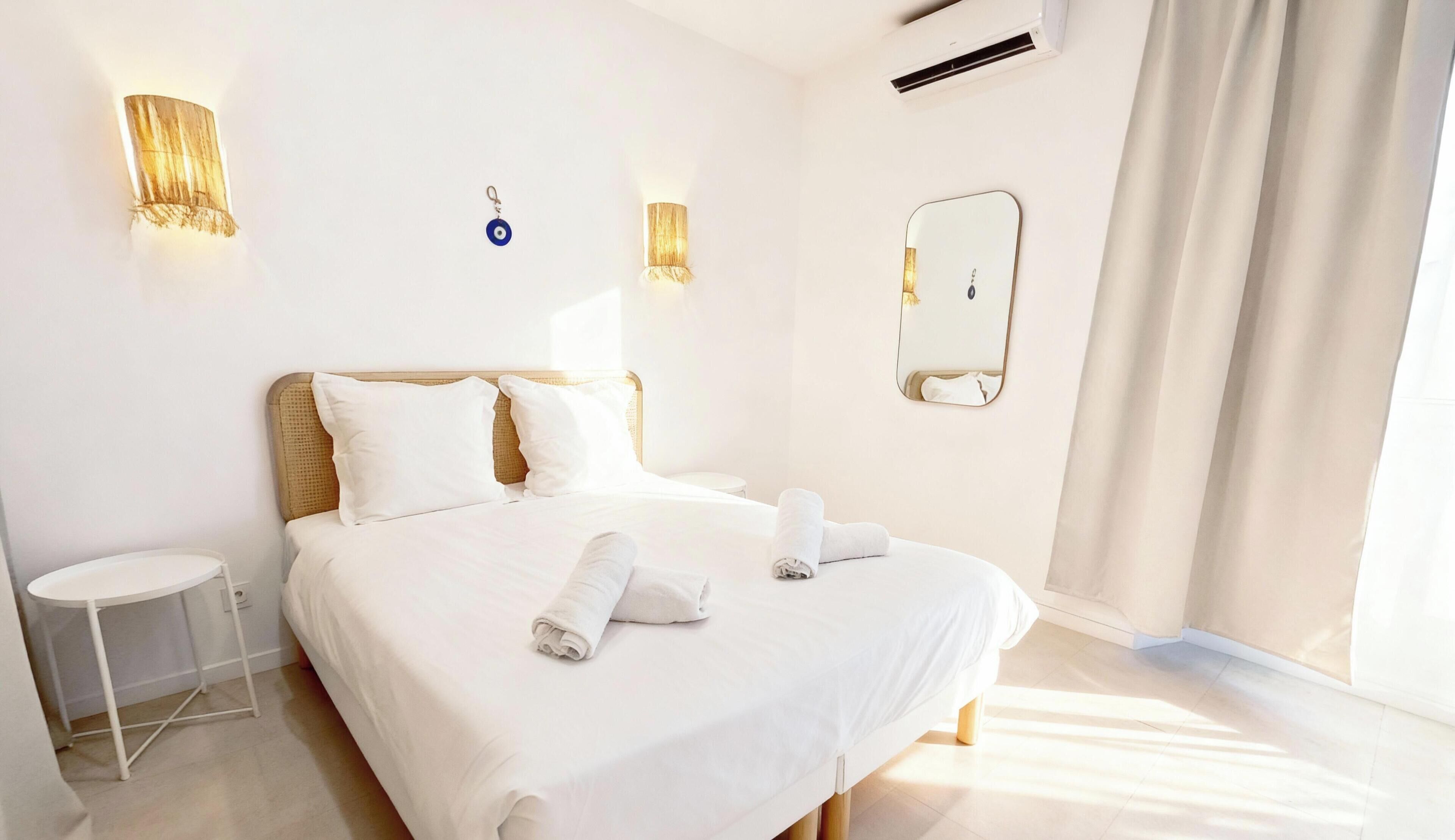 A hotel room with a bed, two bedside tables, a wall-mounted mirror, and a window with curtains.