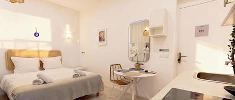 A hotel room with a bed, a small table with chairs, a mirror, a sink, and a KOS sign.