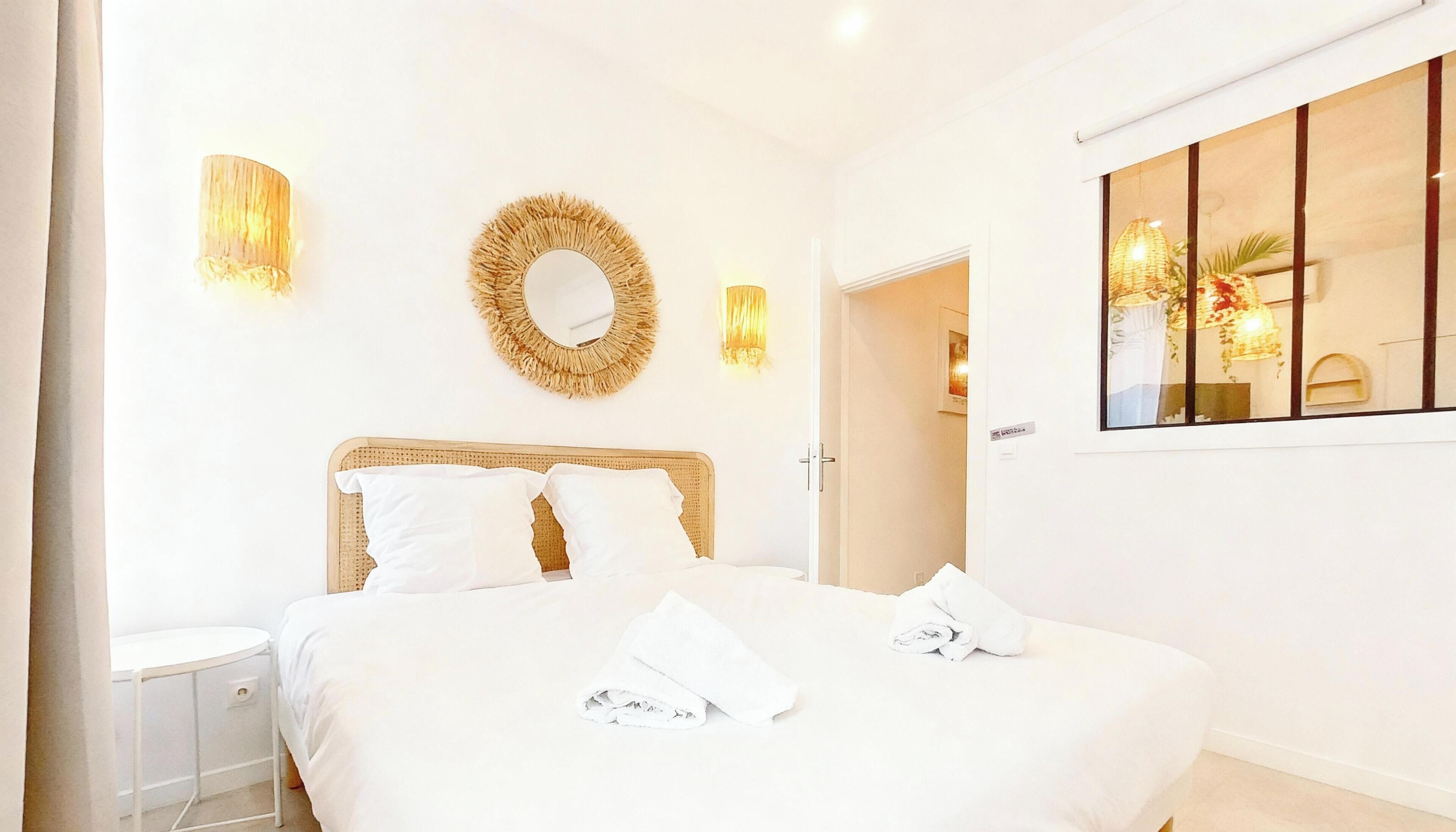A hotel room with a bed, a bedside table, a mirror, and wall-mounted lights.