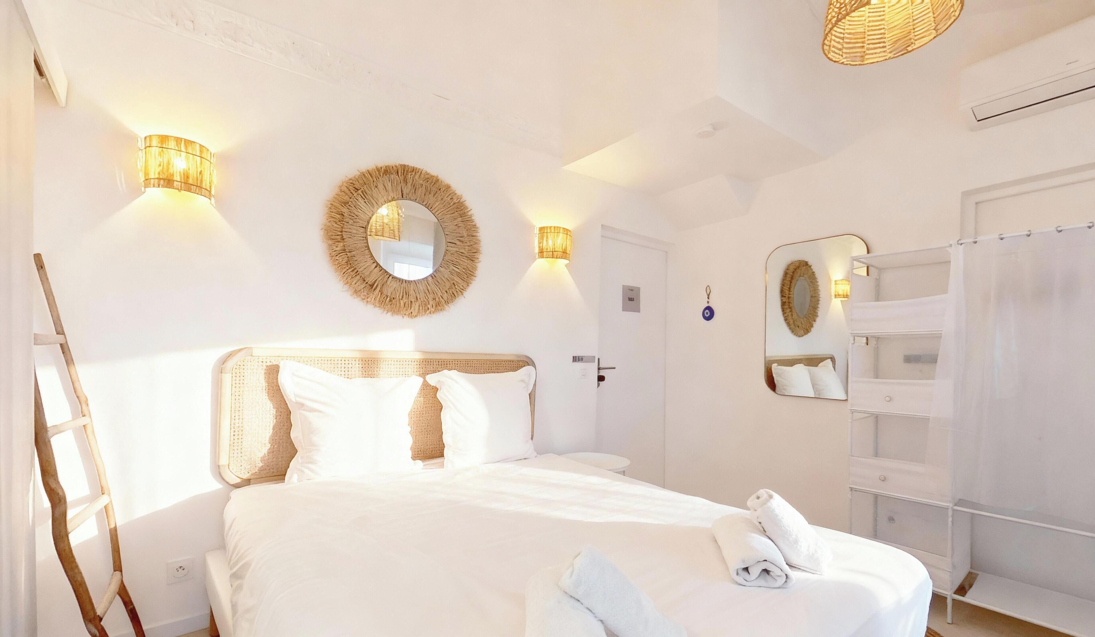 Une chambre à coucher blanche avec un lit, deux miroirs fixés au mur et une armoire.