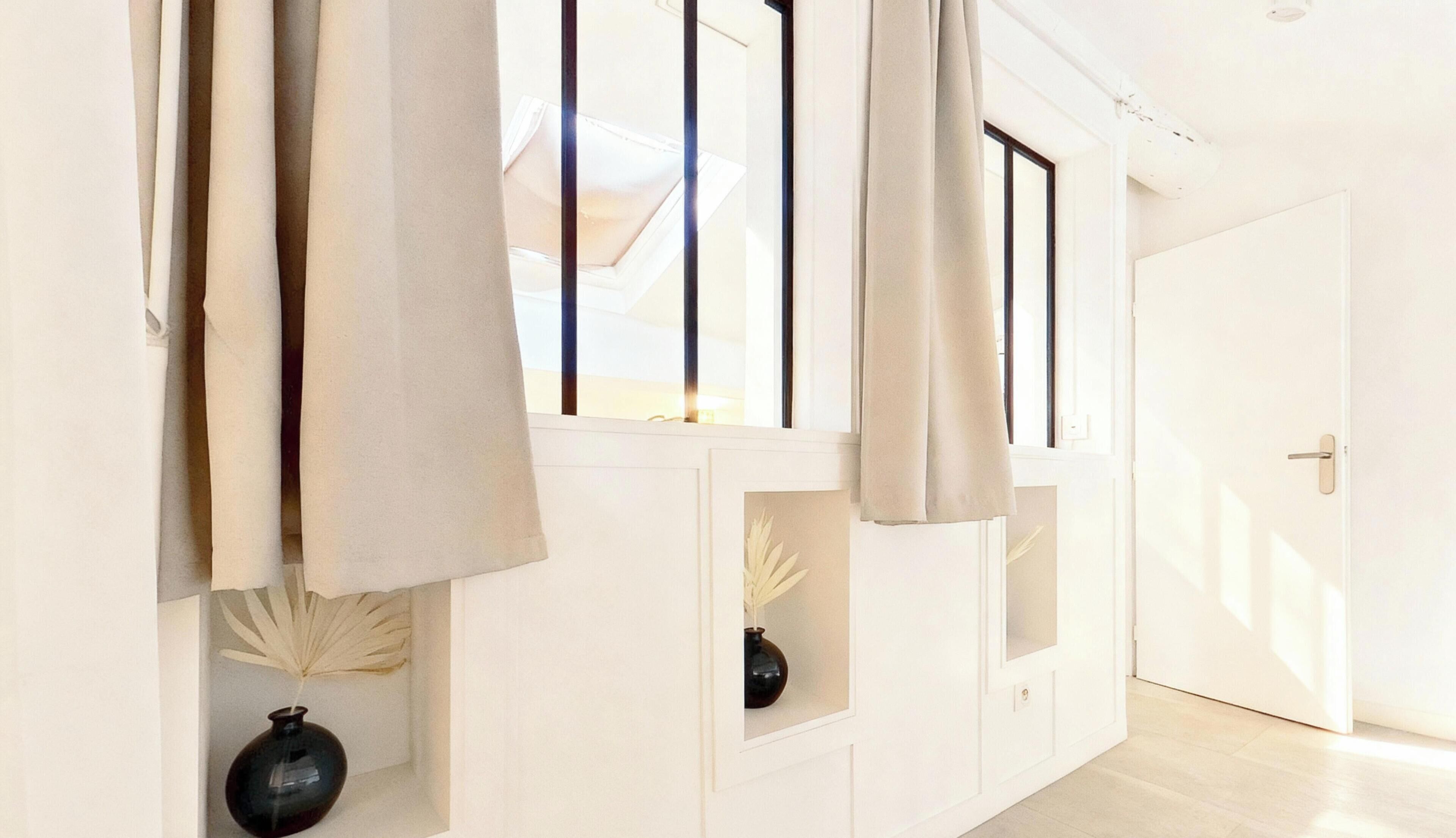 Een lichte, minimalistische hal met witte muren, een houten vloer en een deur aan het einde.