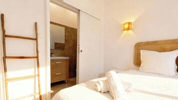 Un dormitorio con cama, una lámpara de noche, una escalera de madera y un baño visible a través de una puerta abierta.