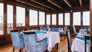 Un comedor con mesas y sillas, ventanas amplias y techo de madera.